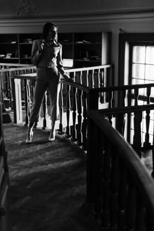 Stylish young lady in glasses posing on balcony at the library. Black and white photoの写真素材