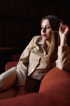Portrait of beautiful stylish young lady in suit sitting on the red sofa.の写真素材