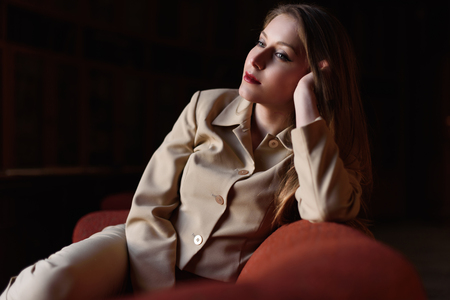 Portrait of beautiful stylish young lady in suit sitting on the red sofa.の写真素材