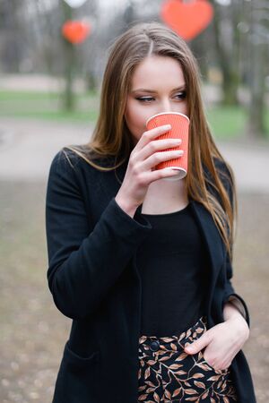 Portrait of young beautiful stylish girl drinking coffee in the park.の写真素材