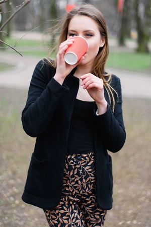 Portrait of young beautiful stylish girl drinking coffee in the park.の写真素材