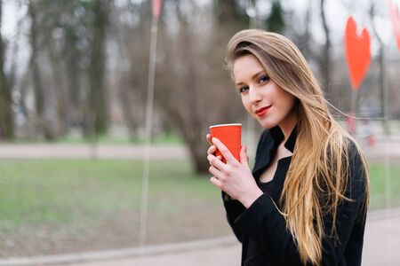 Portrait of young beautiful stylish girl drinking coffee in the park.の写真素材