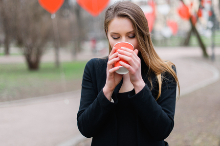 Portrait of young beautiful stylish girl drinking coffee in the park.の写真素材
