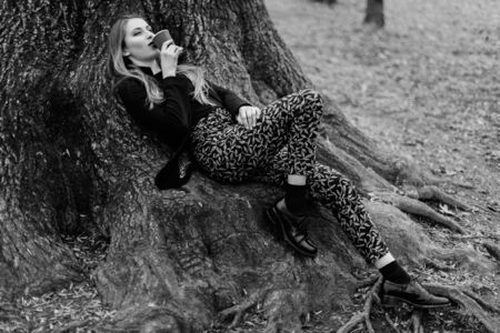 Stylish young girl lying on the tree roots in spring park. Black and white.の写真素材