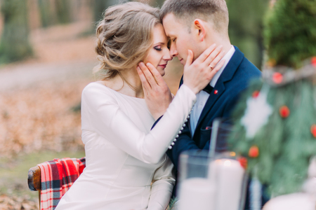 Charming wedding couple softly stroking face of each other at the holiday table in autumn forest.の写真素材