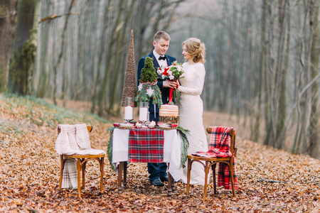 Happy young wedding couple near the decorated table for Christmas holidays in autumn forestの写真素材
