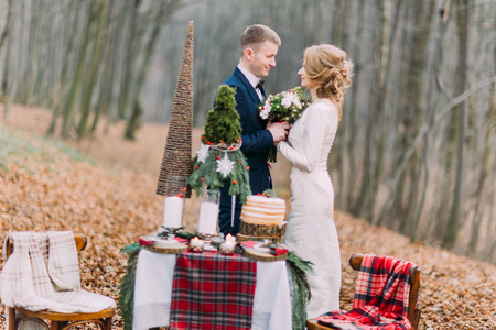 Happy young wedding couple holding hands near the decorated table for Christmas holidays in autumn forestの写真素材