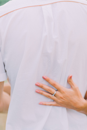 Close of hands of attractive young couple on a date walking together in park, hugging each other around the waist, back view.の写真素材