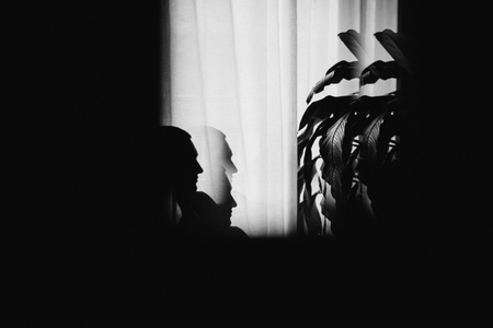 Mysterious man sitting with shadows by the window. Dark background.の写真素材