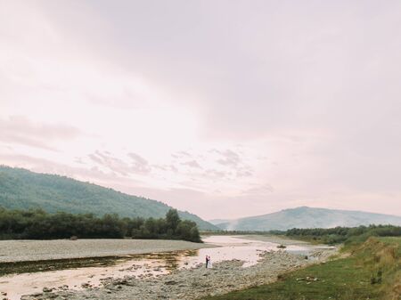 Beautiful wedding couple embracing near the shore of a mountain river with stones.の写真素材