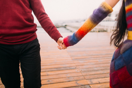 Beautiful young bright happy couple in love holding hands on the berth close up. Sea background.の写真素材
