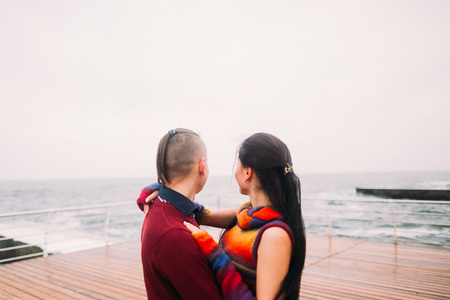 Beautiful bright couple dreamily look into the sea. Rainy autumn day, romantic honeymoon.の写真素材
