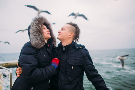Lovers softly holding hands on the pier and seagulls at background. Romantic honeymoon in the wintertime.の写真素材