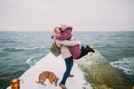 Mother and daughter happy to spend time together. Their little pet dog on the foreground. Winter holidays, sea background.の写真素材