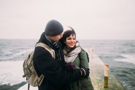 Side view portrait of happy romantic urban fashion couple on pier against the winter sea. Wonderful honeymoon at the seaside.の写真素材