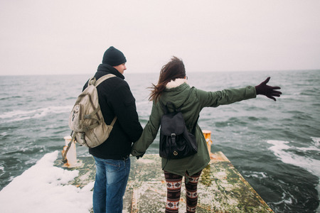 Romantic young loving couple posing on a pier back view, winter sea landscape on background. Beautiful honeymoon at the seaside.の写真素材