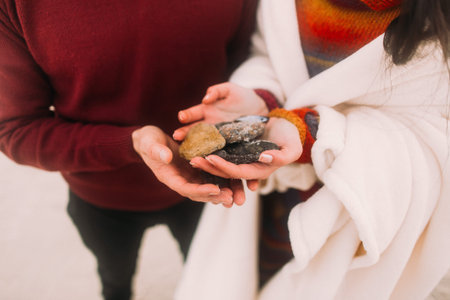 Colorful sea pebbles in couple's hands close up. Happy young couple at the winter beach wrapped in white blanket. Romantic concept.の写真素材