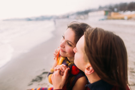 Close up face portrait of beautiful young couple in love sitting on the beach and kissing.の写真素材