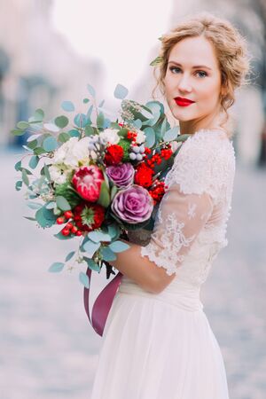 Attractive blond bride with huge bouquet of roses and peonies looks into the camera.の写真素材
