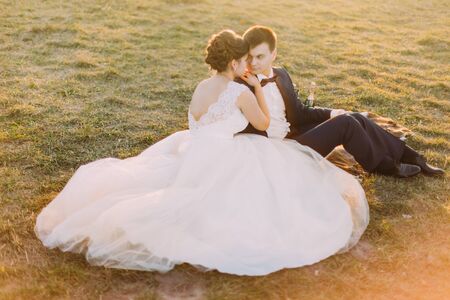 Beautiful bride and groom sitting on blanket plaid with champagne  near old mansion at sunset.の写真素材