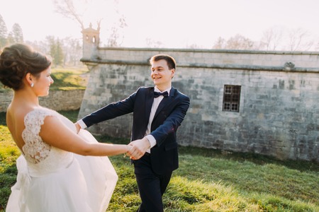 Beautiful young bride and handsome groom dancing outdoors near old mansion at sunset.の写真素材