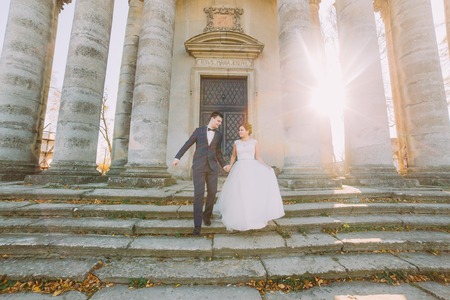 Romantic married couple bride and groom walking down stairs antique builing background.の写真素材