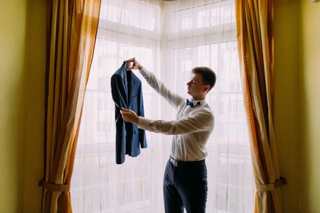 Young man in white shirt and bow-tie holds  business jacket coat.の写真素材