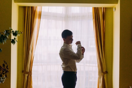 Elegant young fashion man in tuxedo looking at his cufflinks while fixing them.の写真素材