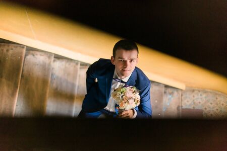 Portrait of happy man in blue suit on the stairs smiling holding bouquet. The view from the top.の写真素材