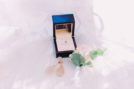 Bride's earrings and golden wedding ring in box over white background.