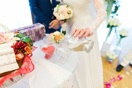 The bride and groom perform a ritual ceremony of sand - pour colorful sand from two different vessels in a common wedding traditionsの写真素材