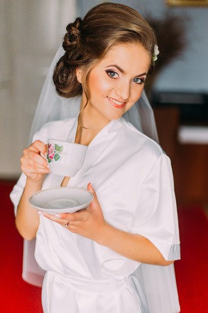 Portrait of beautiful bride posing in robe with cup on the wedding morning.の写真素材