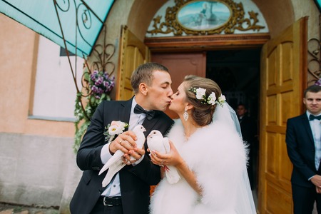 Happy newlyweds bride and groom with doves in hands on church doors background.の写真素材