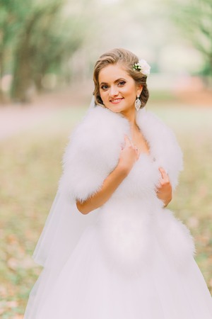 Portrait of happy blonde bride in white dress and fur boa on the lane at the autumn park.の写真素材