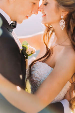 Close-up photo of newlywed young bride and groom with flower bouquet rubbing noses outdoors.の写真素材