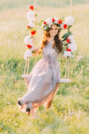 Attractive blonde beauty in lilac dress and wreath on a flower swing in garden.の写真素材