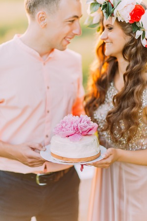 Couple celebrating at picnic, young man and woman holding cake decorated with pink flowers.の写真素材