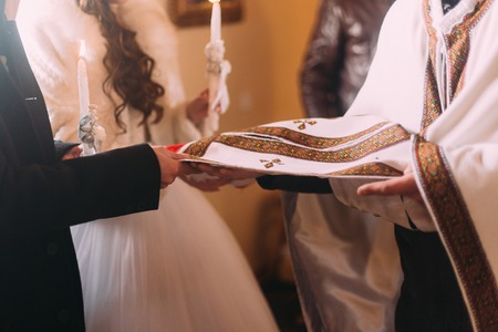 Wedding ceremony of happy elegant bride and stylish groom, holding candles in the old church.の写真素材