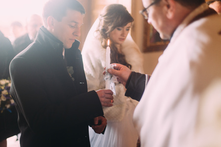 Wedding ceremony of happy elegant bride and stylish groom, holding candles in the old church.の写真素材