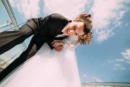 Smiling bride and groom posing for the camera against blue sky with clouds, view from below.の写真素材