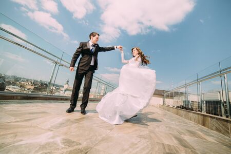 Photo of beautiful bride and groom dancing on roof top at sunny day.の写真素材
