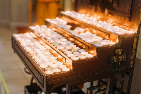 Votive candles in a rack burninng in ancient cathedral.の写真素材
