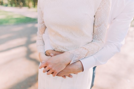 Close-up photo of bride and groom in embrace holding hands on her stomach.の写真素材