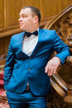 Handsome elegant groom posing looking towards on old wooden stairs at the background of luxury interior.の写真素材