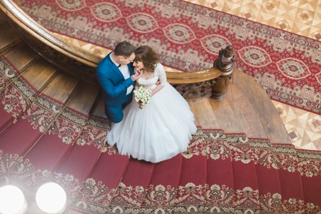 Luxury bride and handsome elegant groom on old wooden stairs at the background of luxury interior. The view from the top.の写真素材