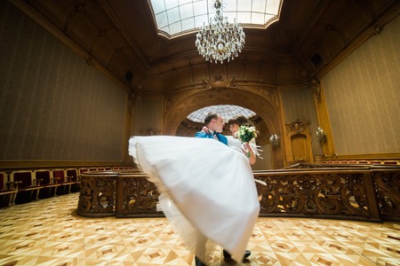 Elegant wedding couple dancing at vintage house in the front of old stained-glass ceiling. Groom carrying his wife with bouquetの写真素材