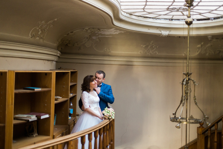 Pretty bride in white dress and groom wearing blue suit posing and looking at glass ceiling.の写真素材