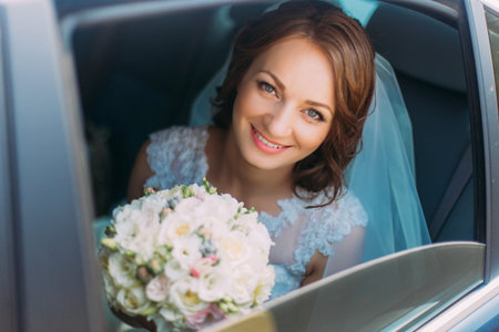 Happy smiling bride with flower bouquet siting in the car.の写真素材