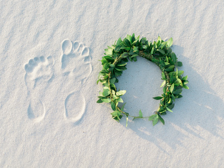 Footprint and green laurel wreath on white sand tropical beach.の写真素材