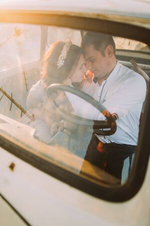 Portrait of a young girl with floral headband and handsome man sitting in a vintage car and smiling face-to-face.の写真素材